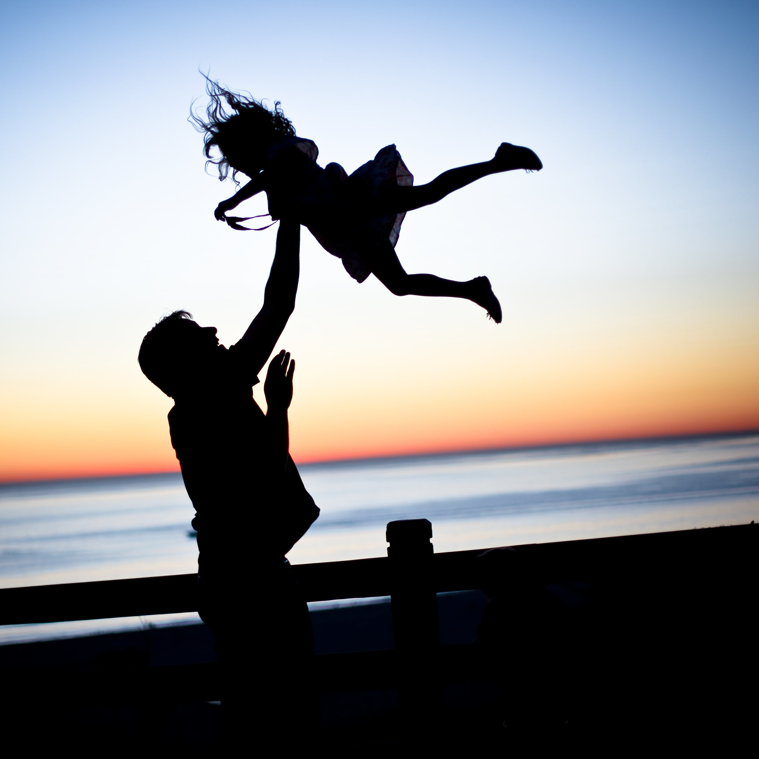 a silhouette of a man throwing a child up in the air