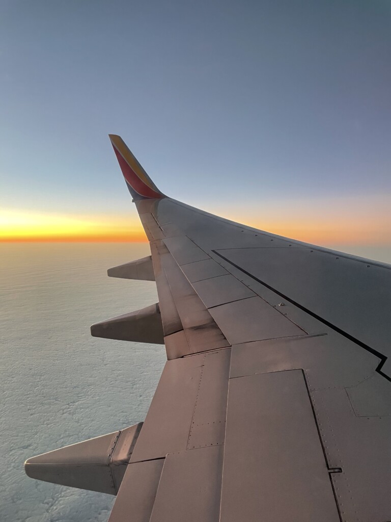 an airplane wing with the sun setting in the background