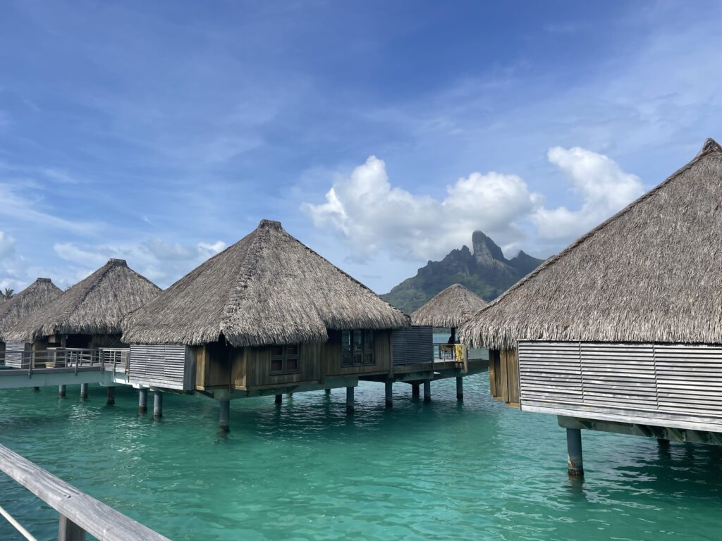 a group of huts on stilts over water with Bora Bora in the background