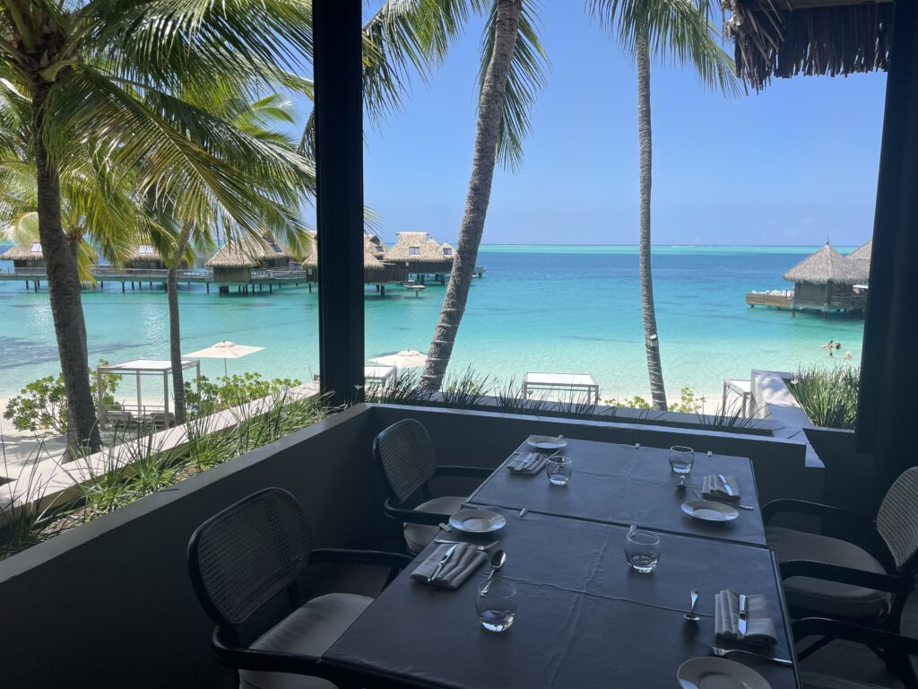a table set up for a meal with a view of the ocean and a hut