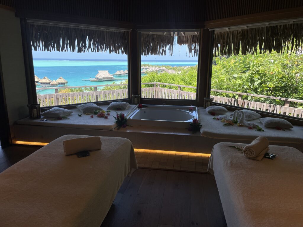 a room with a tub and beds and a view of the ocean