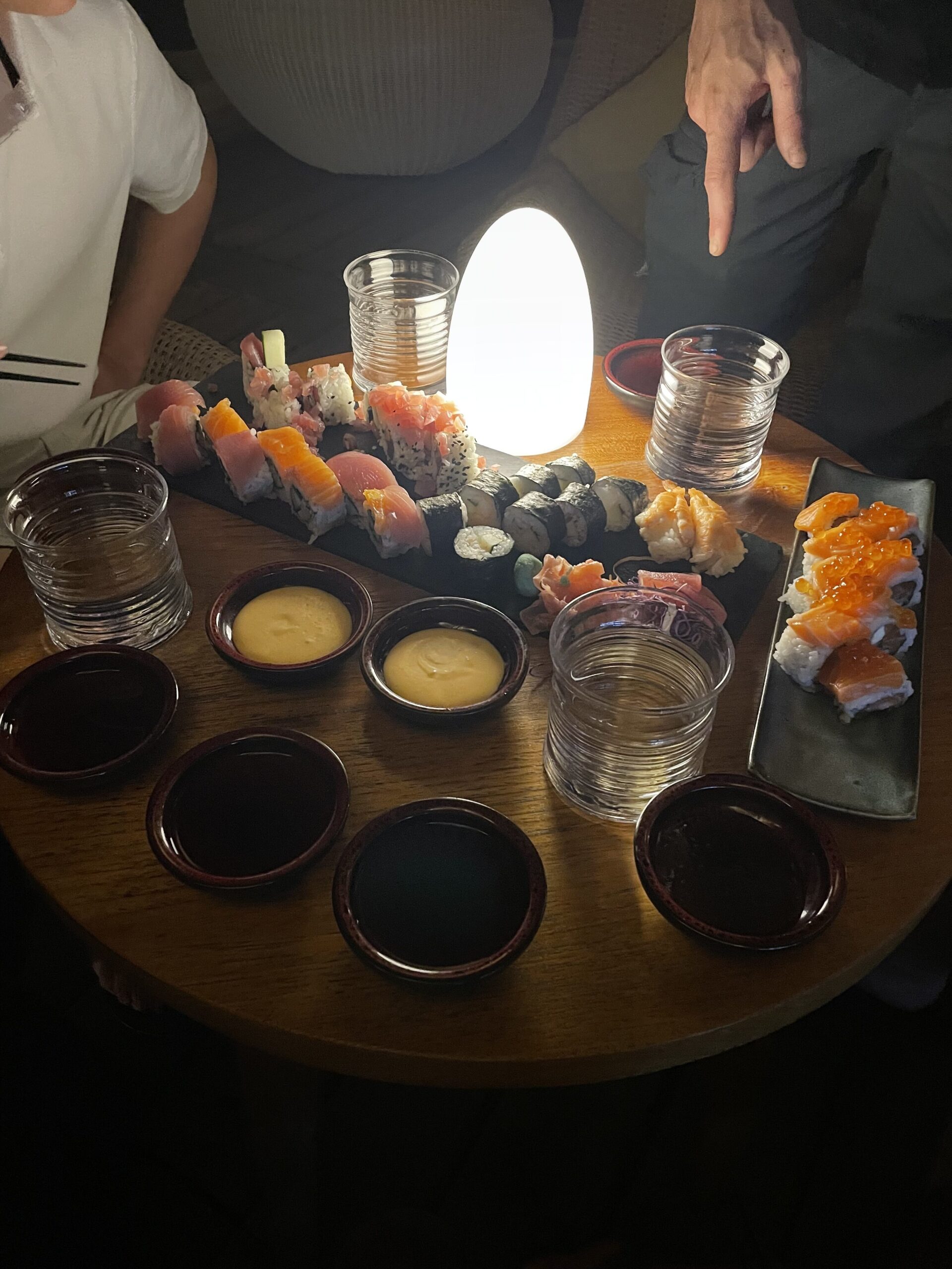a table with a plate of sushi and glasses of sauce