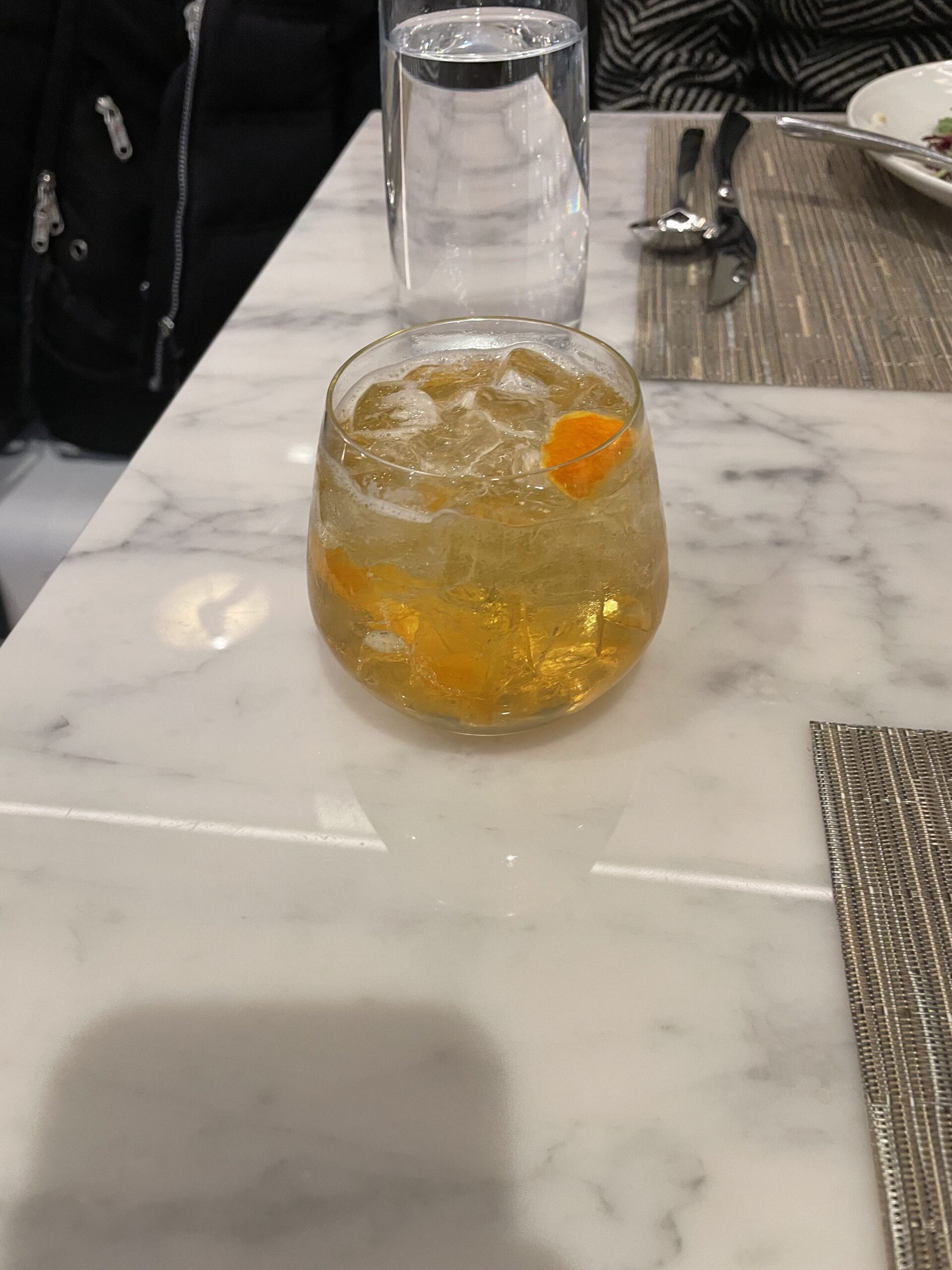 a glass of liquid with ice and orange slice on a marble table