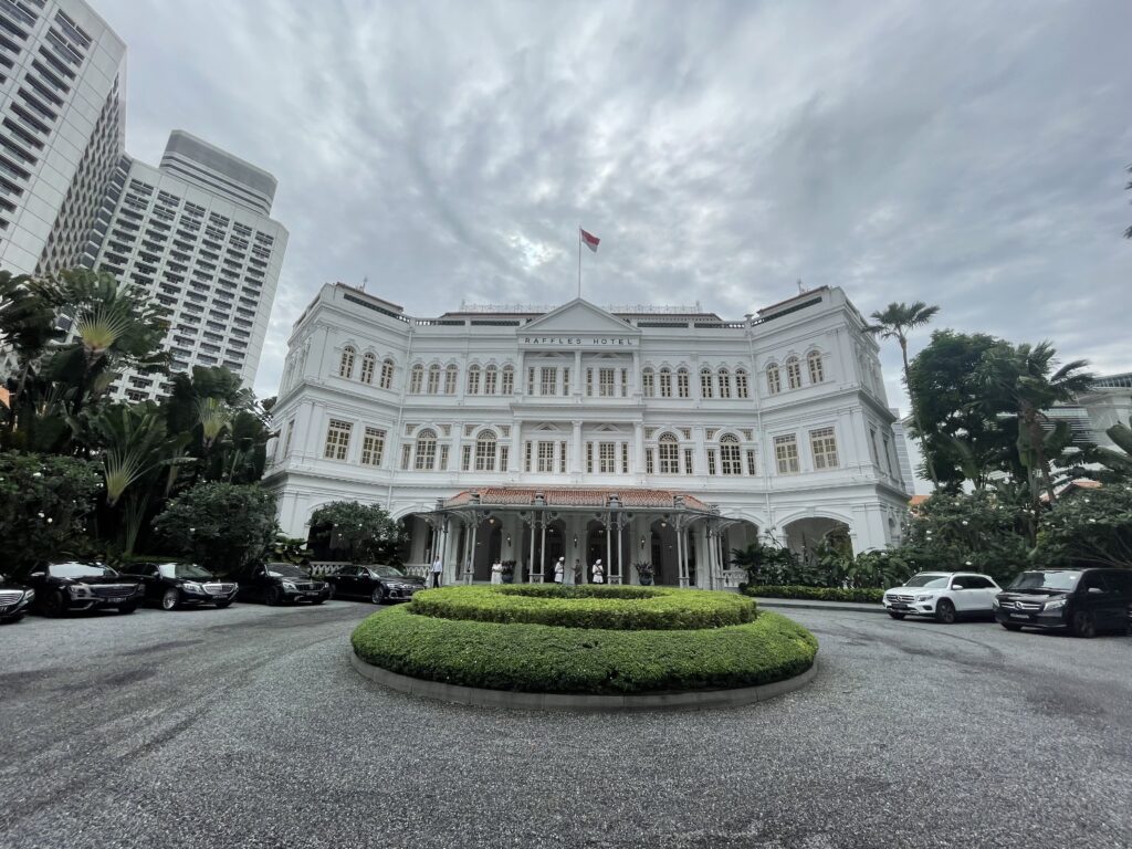 a white building with a round circular lawn and a car in front with Raffles Hotel in the background